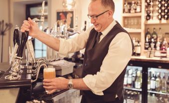 a man in a vest is pouring beer from a tap into a glass at a bar at The New Inn - Yealand