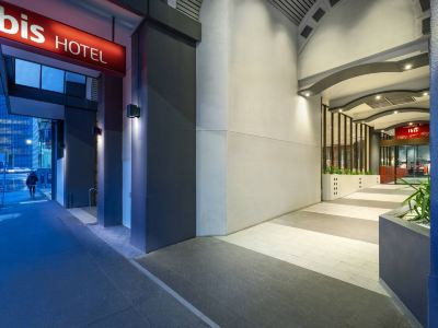 "a modern hotel entrance with a sign that reads "" hotel "" and a red bench at the end" at Ibis Melbourne Hotel and Apartments