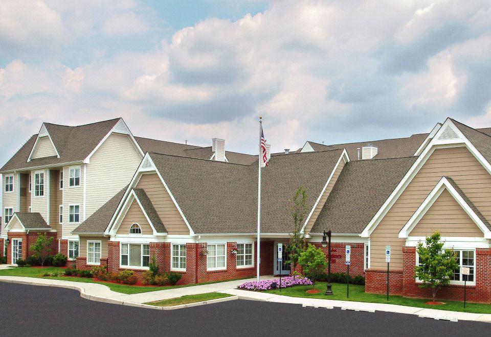 a large red brick building with an american flag flying in front of it , surrounded by trees at Residence Inn Cranbury South Brunswick