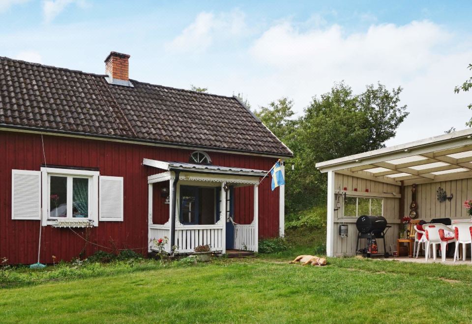 a red house surrounded by a lush green lawn , with a barbecue grill and chairs on the porch at Vadstena