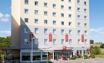 a modern building with multiple floors , balconies , and red banners on the facade , set against a clear blue sky at Ibis Luxembourg Sud