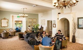 a group of people are sitting on couches and chairs in a room with chandeliers at Mercure Bristol North the Grange Hotel