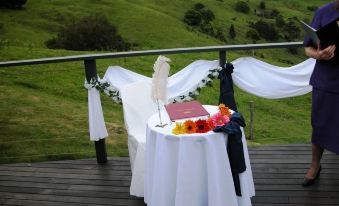 a table with a white cloth and flowers is set up on a wooden deck overlooking a green field at Top of the Hill