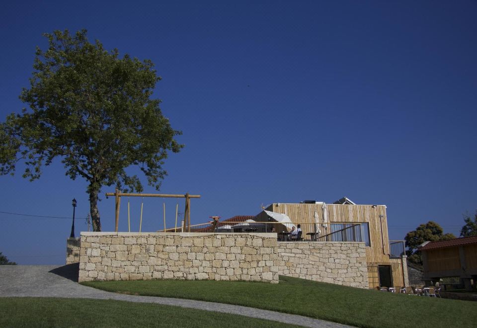 a wooden building with a stone wall and green grass , under a clear blue sky at Casa de Lobos