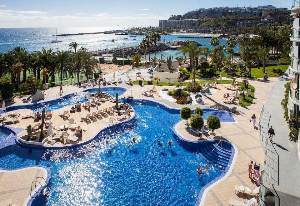 a large , blue swimming pool with people in it and palm trees surrounding the water at Radisson Blu Resort, Gran Canaria