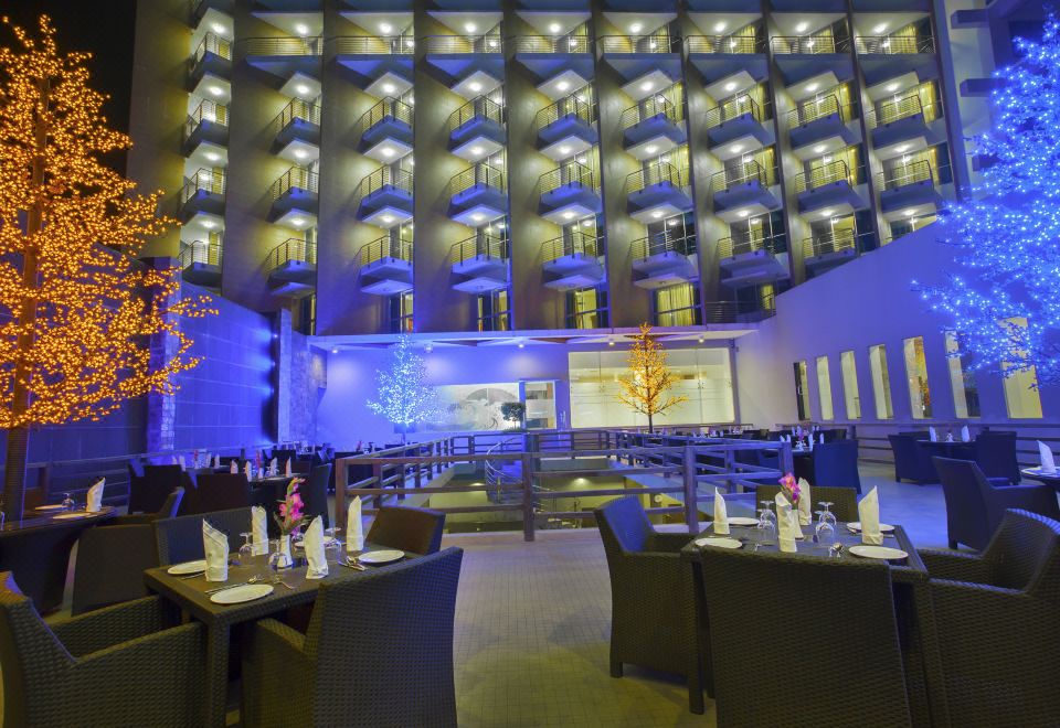 a large , modern hotel lobby with multiple tables and chairs set up for dining , illuminated by colorful lights at Long Beach Hotel