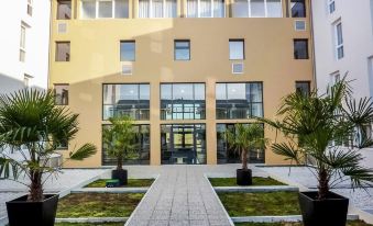 a modern building with a green courtyard and palm trees in front , under a clear blue sky at Comfort Suites Pau Idron