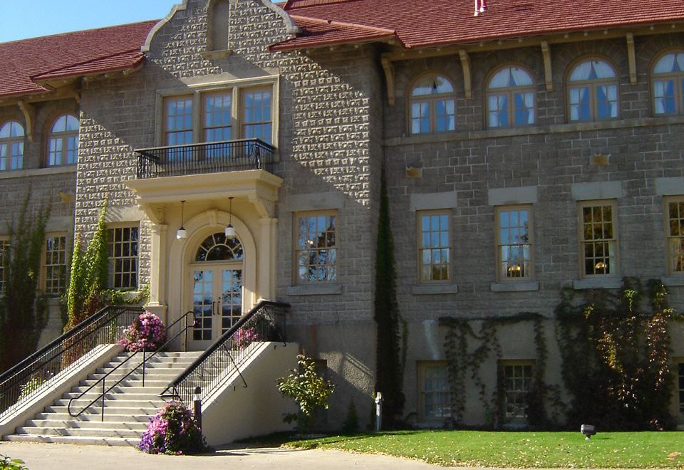 a large stone building with a red roof and two towers , surrounded by greenery and flowers at St. Eugene Golf Resort & Casino