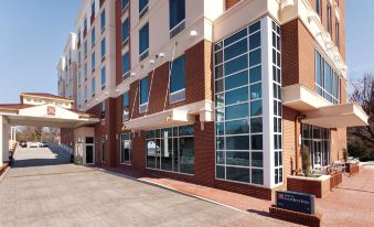 a modern , white - walled building with large windows and red - brick accents , situated on a sunny day at Hilton Garden Inn Falls Church
