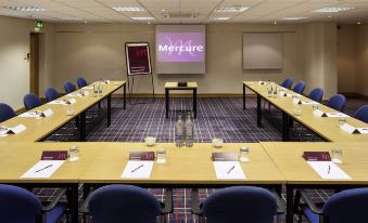 "a conference room with several tables and chairs , a projector screen , and a projector screen displaying the word "" mercure ""." at Mercure Hull Grange Park Hotel