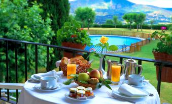 a table is set with breakfast items , including fruit and pastries , on a balcony overlooking a pool and mountains at Parador de Verin