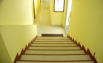 a long , narrow hallway with yellow walls and a white tiled floor leads to an open door at Sirasit 999 Mansion