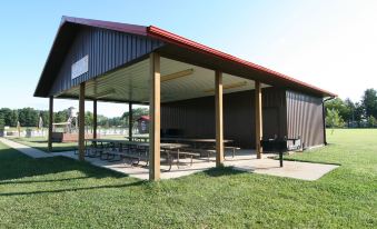 a large , open metal building with a red roof and wooden beams , surrounded by picnic tables and benches at Indiana Beach Accommodations