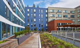 a modern building with multiple windows and balconies , surrounded by wooden walkways and greenery , under a clear blue sky at Aloft Seattle Redmond