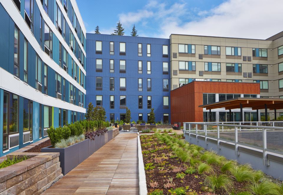 a modern apartment building with blue and brown exterior , surrounded by a lush green garden with flowers at Aloft Seattle Redmond