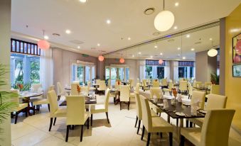 a large dining room with white tables and chairs , a red light fixture on the ceiling , and a view of the ocean through the windows at Thistle Port Dickson Resort