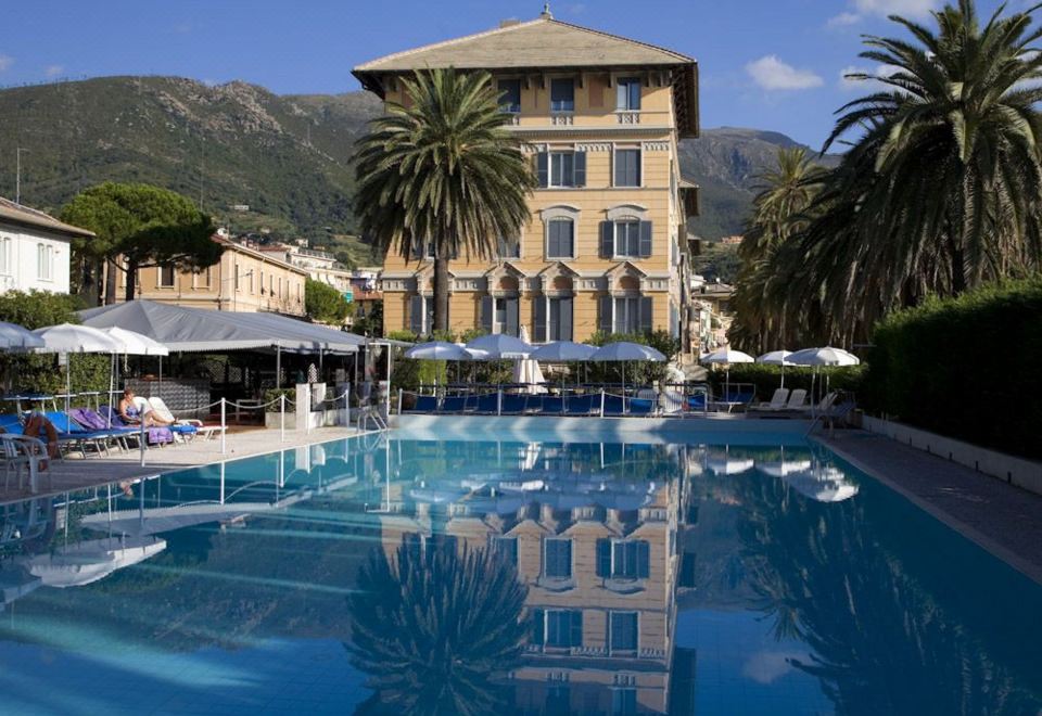 a large outdoor swimming pool surrounded by a building , with palm trees in the background at Grand Hotel Arenzano