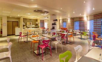 a brightly colored dining room with several tables and chairs arranged for a group of people at Ibis Clermont-Ferrand Sud Carrefour Herbet