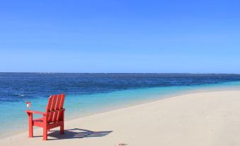 a red adirondack chair is sitting on a sandy beach , overlooking the ocean with clear blue water at Stevensons at Manase