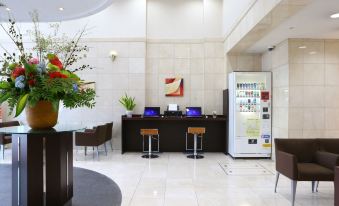 a modern hotel lobby with a reception desk , two chairs , and a vase of flowers at Hotel Hokke Club Kumamoto