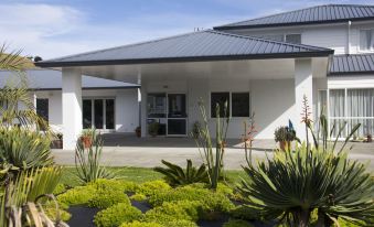 a white house with a covered porch , surrounded by a lush green garden filled with various plants and flowers at Motel Oasis