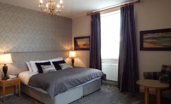 a large bed with gray bedding is in a room with purple curtains and a chandelier at The George at Baldock