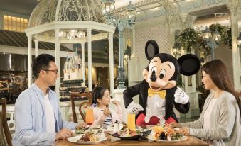 A couple is sitting at a table with food and drinks in front of them, with one person holding up the items at Hong Kong Disneyland Hotel