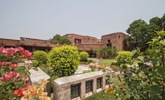 a large brick building surrounded by lush greenery and flowers , creating a serene and picturesque setting at Faisalabad Serena Hotel
