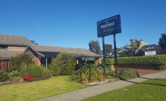 a brick house surrounded by a lush green lawn , with a sign in front of it at The Heritage Bendigo