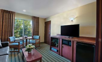 a living room with a flat screen tv , coffee table , and blue chairs near a window at Oxford Suites Pendleton