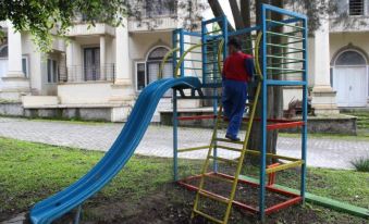 a person climbing a colorful jungle gym in a park with trees and buildings in the background at Villa Berastagi Highland