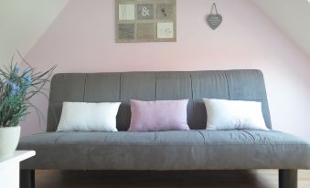 a grey couch with three white pillows is placed in a room with pink walls and a light - colored wood floor at La Grenouillère