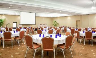 a large conference room with round tables and chairs , a projector screen , and a podium at Pelican Waters Resort