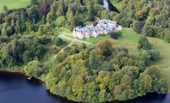 aerial view of a large mansion surrounded by trees and grass , with a lake in the background at Glengarry Castle Hotel