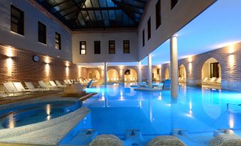 a large indoor swimming pool surrounded by lounge chairs , with people relaxing and enjoying the space at Castilla Termal Olmedo