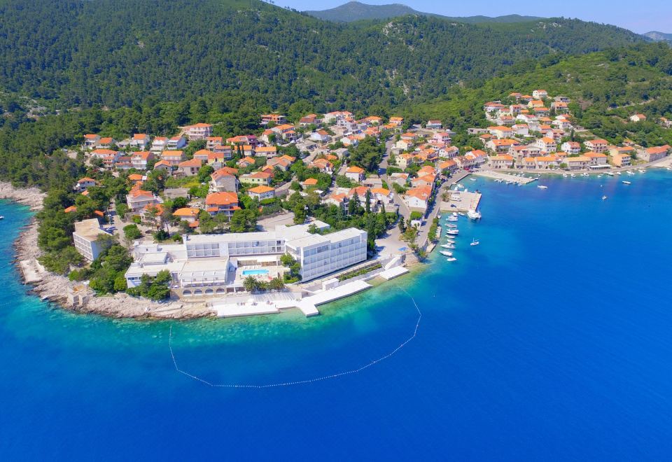 aerial view of a small coastal town surrounded by blue water and green hills , with a yacht docked nearby at Aminess Lume Hotel