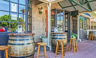 a brick building with wooden barrels on the porch and stools in front of it at Motel Goolwa