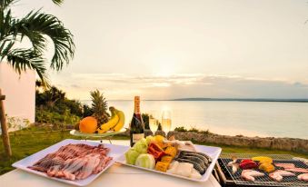 a table with a bottle of champagne , plates of fruit and meat , and a basket filled with grapes is set up near the water at Crystal Villa Miyakojima Sunayama Beach