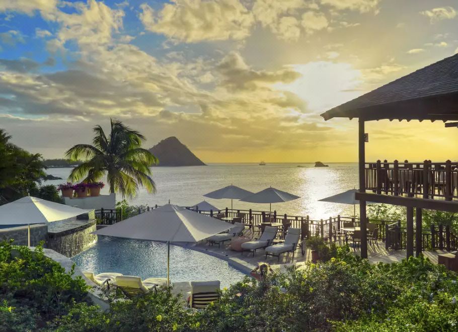 a beautiful tropical resort with a pool , umbrellas , and palm trees overlooking the ocean at sunset at Cap Maison Resort & Spa