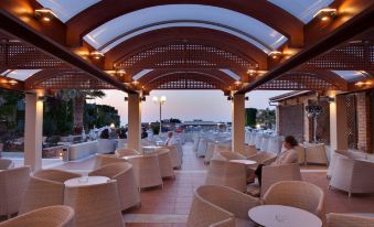 a man sitting in a patio area with white chairs and a wooden ceiling , overlooking a body of water at Bella Beach Hotel