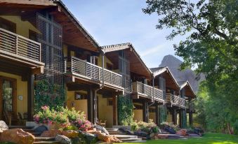 a row of wooden houses with balconies and greenery surrounding them , set against the backdrop of mountains at Desert Pearl Inn