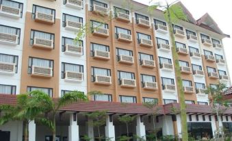 a large building with multiple windows and balconies , situated in a park - like setting under a cloudy sky at Permai Hotel Kuala Terengganu