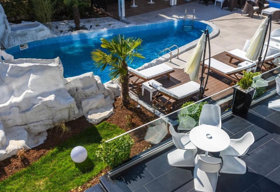 a swimming pool surrounded by lounge chairs and umbrellas , with a palm tree in the background at Hotel Mirror Skopje