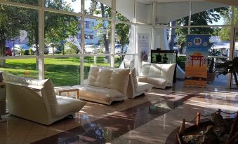 a spacious living room with several white couches and chairs arranged in front of a large window , allowing natural light to fill the space at Academy Hotel