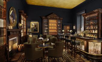 a luxurious living room with dark blue walls , gold ceiling , and a large bookshelf filled with various books at The Langley, a Luxury Collection Hotel, Buckinghamshire
