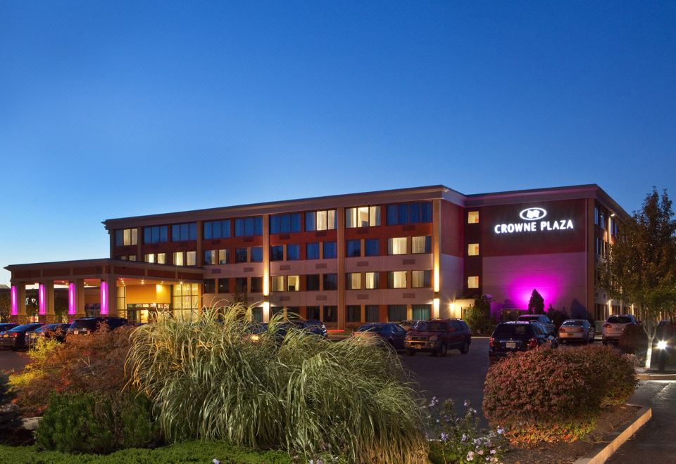 a large hotel building with a parking lot in front of it , illuminated by purple lights at Crowne Plaza Boston - Woburn, an IHG Hotel