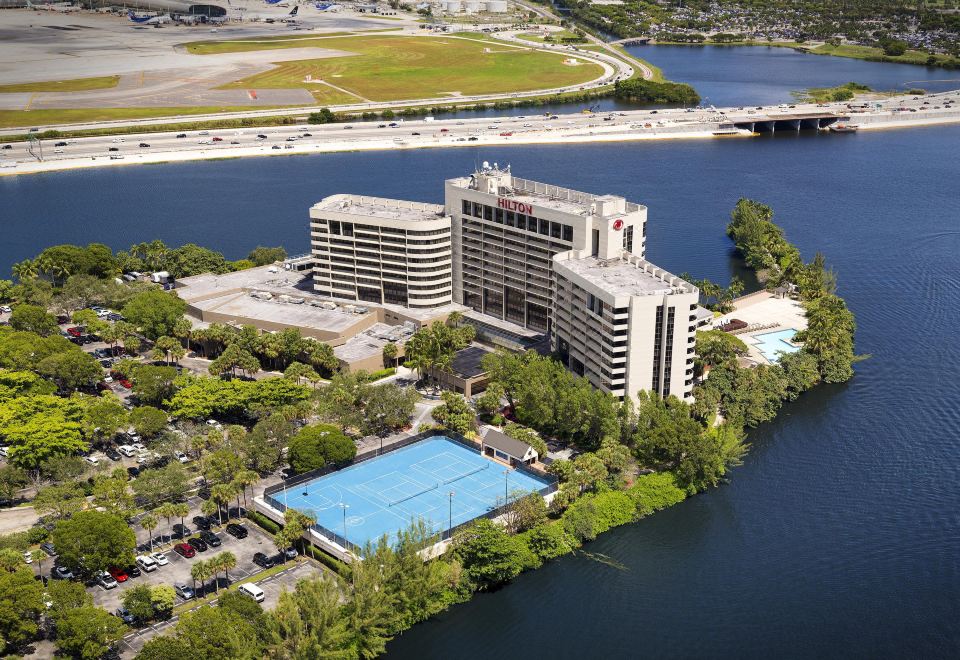 aerial view of a large building surrounded by water , with a tennis court visible in the foreground at Hilton Miami Airport Blue Lagoon