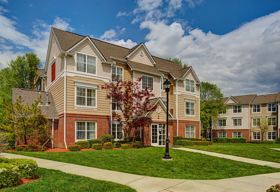 a modern apartment building with multiple floors , surrounded by green grass and trees , under a blue sky at Residence Inn Saddle River