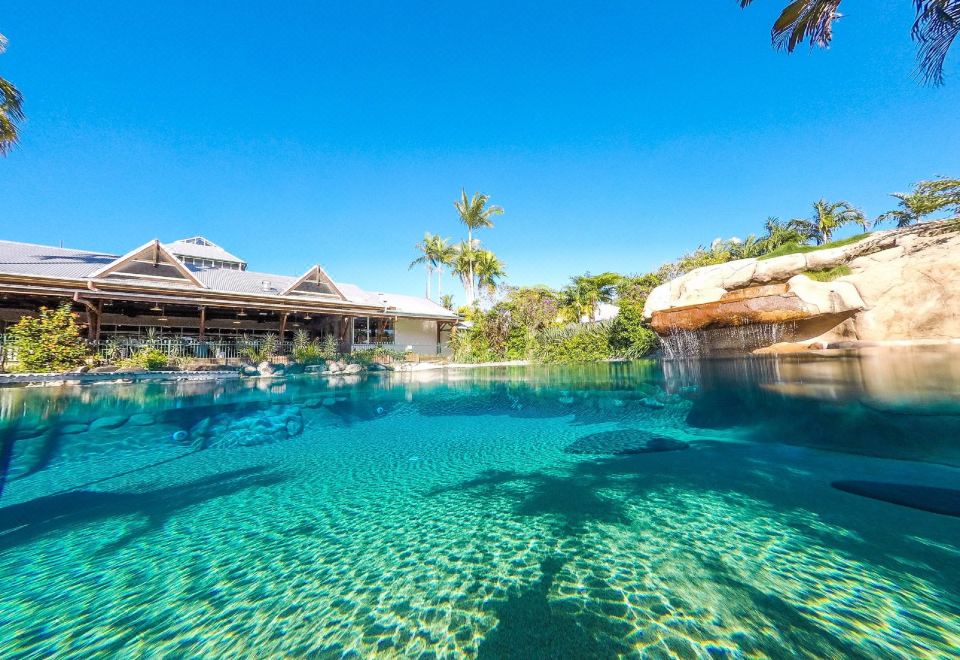 a large outdoor swimming pool surrounded by palm trees , with people enjoying their time in the water at Cairns Colonial Club Resort