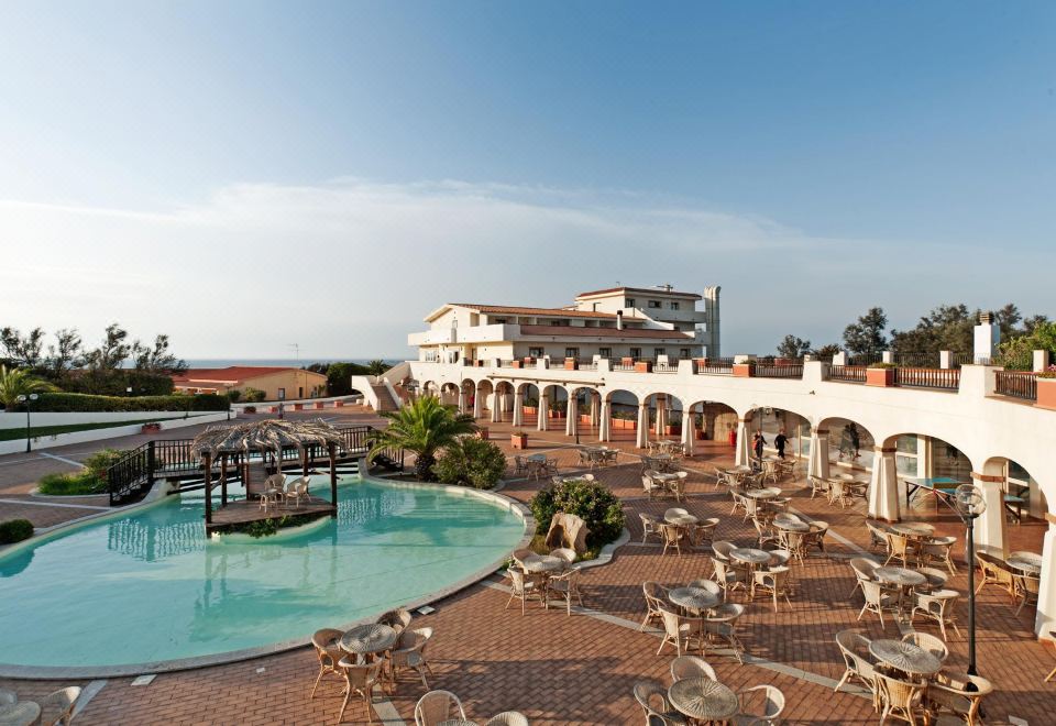 a large swimming pool surrounded by lounge chairs and tables , with a hotel in the background at La Plage Resort